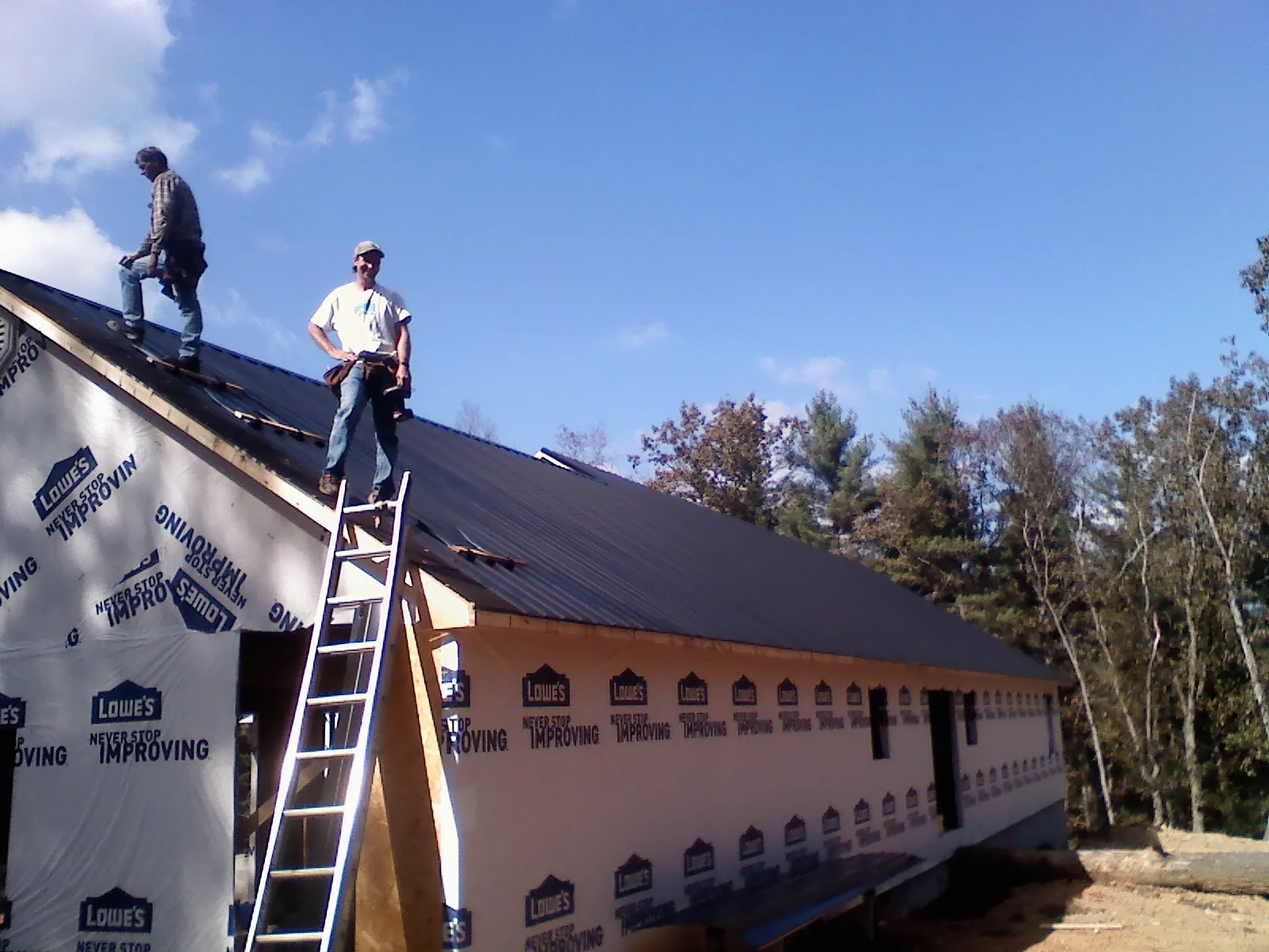 Two roofers standing on a long dark metal roof over a wrapped building in Shelton