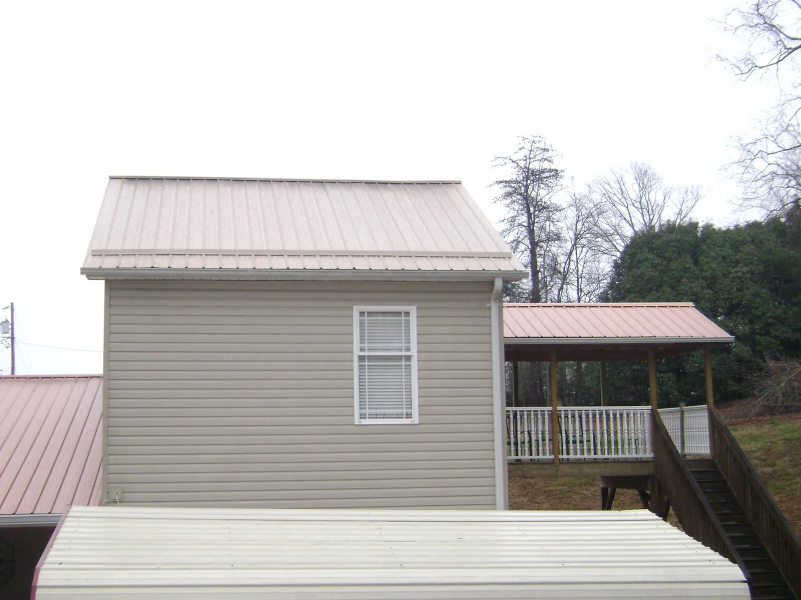Tan metal roofs on a two story addition and attached porch, from a Roof Replacement job in Shelton